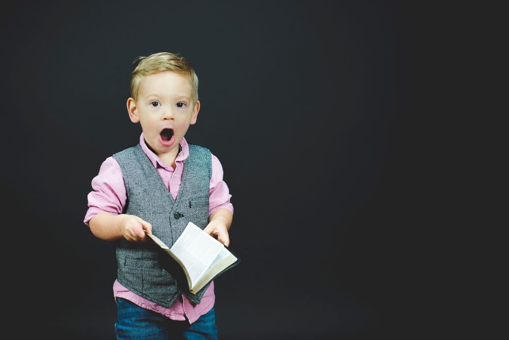 A boy holding a book with his mouth open in wonder.